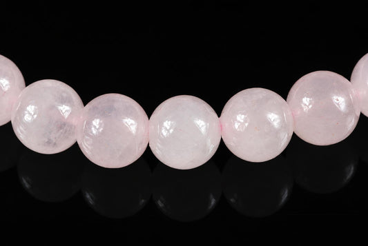A row of round, pale pink beads on a dark surface with reflections.