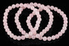 A pink rose quartz bracelet with round beads arranged in loops on a dark reflective surface.