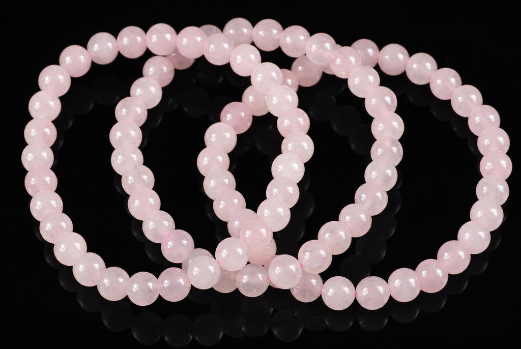 A pink rose quartz bracelet with round beads arranged in loops on a dark reflective surface.