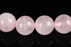 Four round, pale pink beads with a smooth surface and faint internal patterns rest on a dark reflective surface.