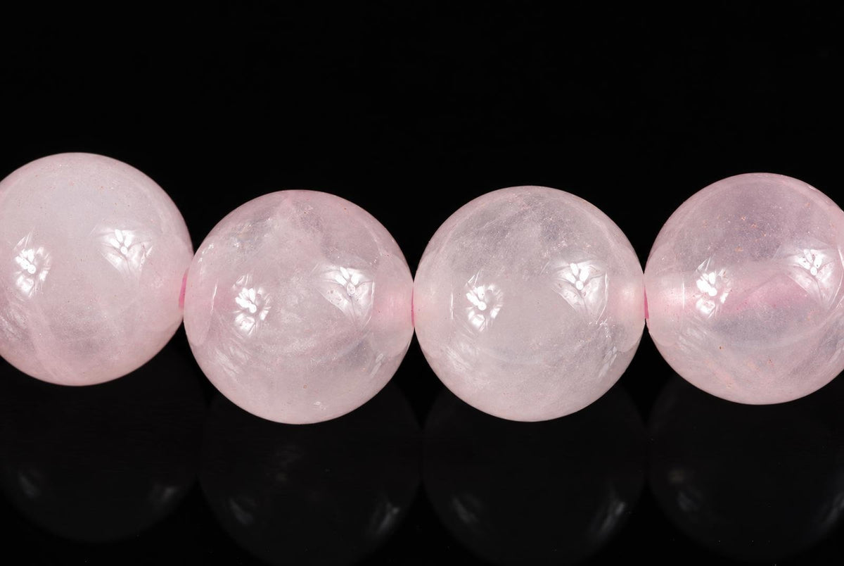 Four round, pale pink beads with a smooth surface and faint internal patterns rest on a dark reflective surface.