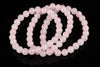 A pink rose quartz bracelet with round beads arranged in loops on a dark reflective surface.