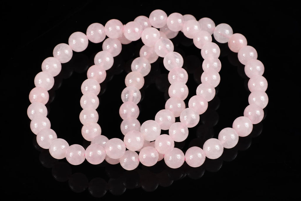 A pink rose quartz bracelet with round beads arranged in loops on a dark reflective surface.