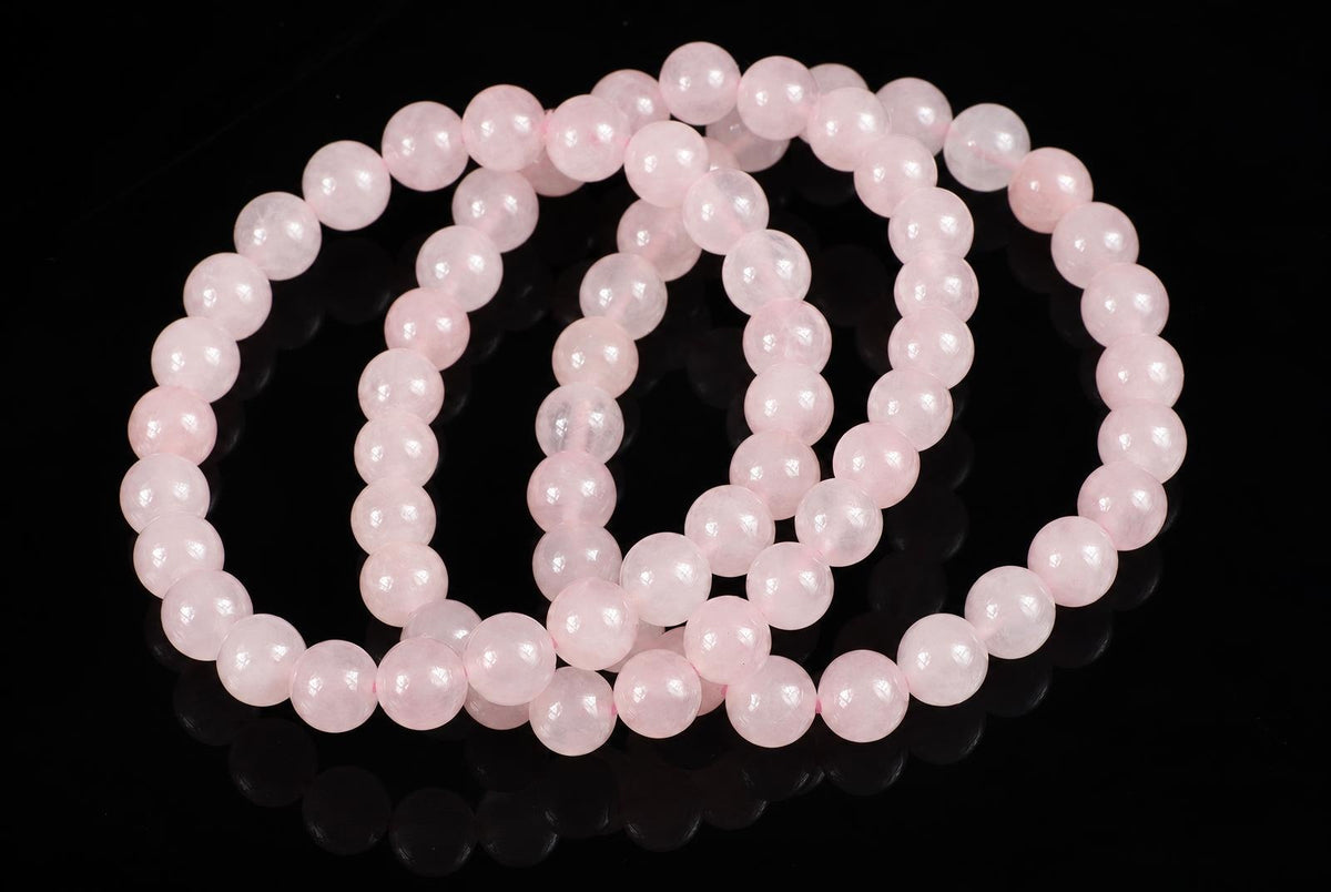 A pink rose quartz bracelet with round beads arranged in loops on a dark reflective surface.