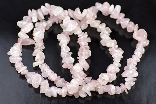 A strand of pale pink rose quartz chips arranged in a loose coil on a dark surface.