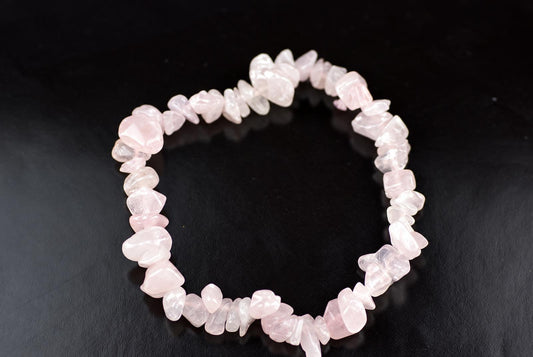 A bracelet made of irregular pink rose quartz chips arranged in a circle on a dark surface.