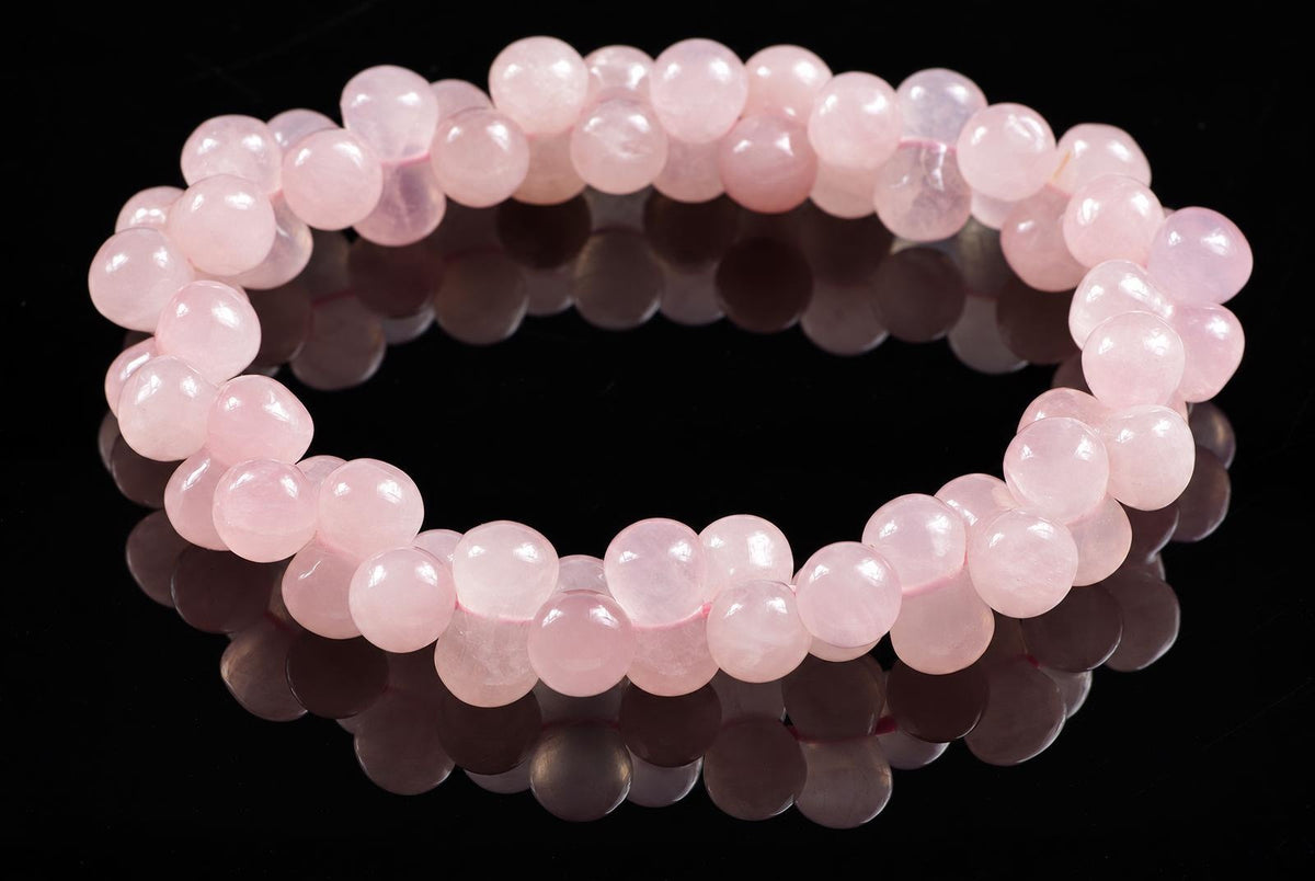 A bracelet of round, pale pink beads on a dark reflective surface.