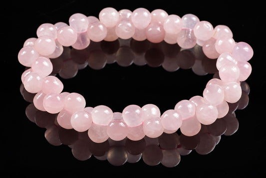 A bracelet of round, pale pink beads on a dark reflective surface.
