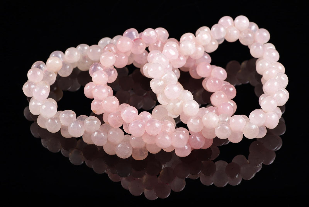 Three pink rose quartz bead bracelets arranged on a dark reflective surface.