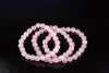 A faceted pink rose quartz bracelet with round beads arranged in a loop on a dark surface.