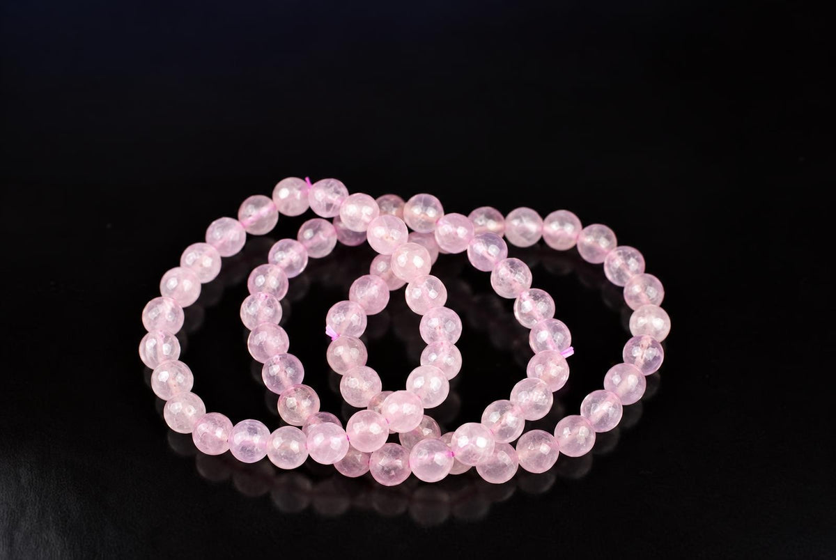 A faceted pink rose quartz bracelet with round beads arranged in a loop on a dark surface.