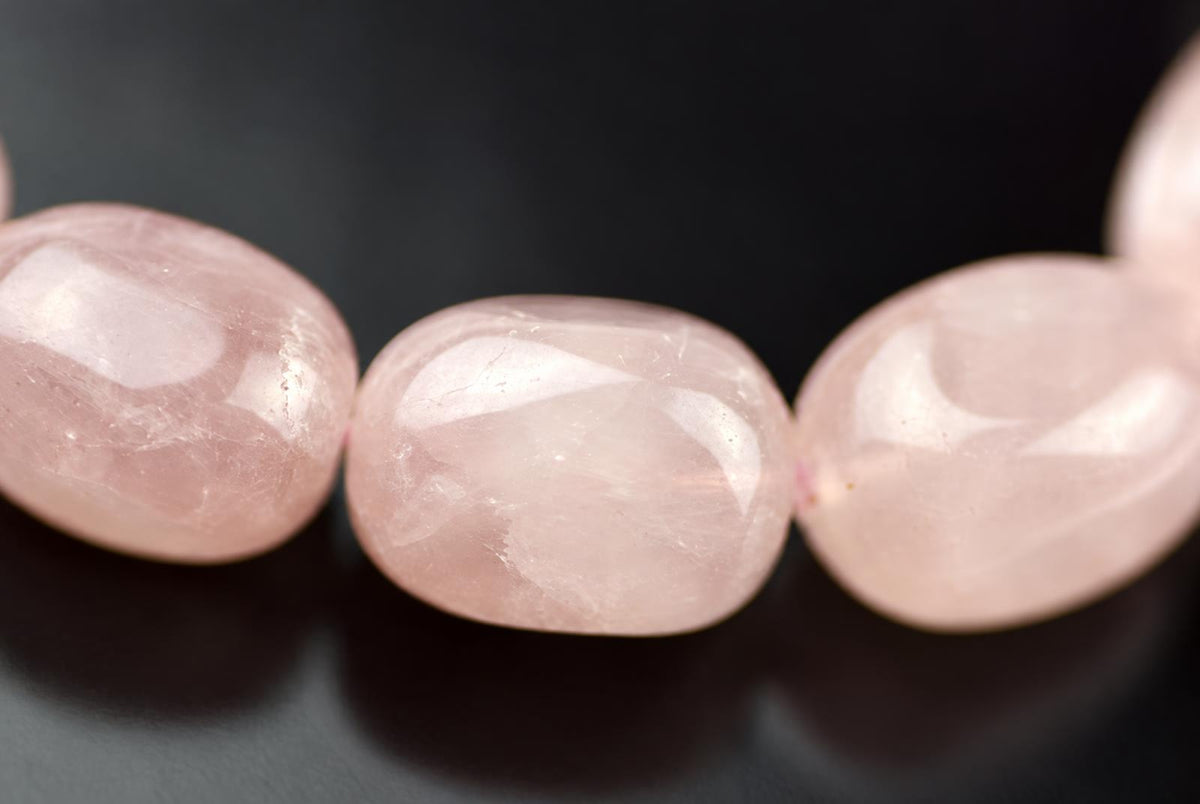 Three smooth, pale pink rose quartz beads with a polished surface rest on a dark surface.