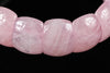 A close-up of a pink rose quartz bracelet with smooth, rounded beads on a dark surface.