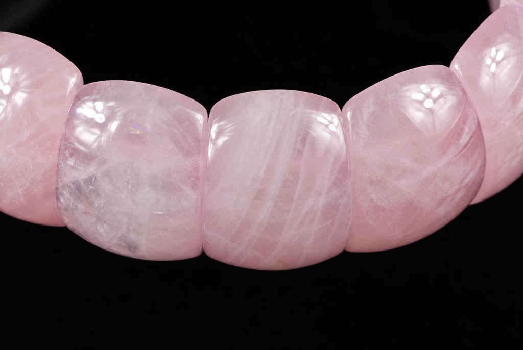 A close-up of a pink rose quartz bracelet with smooth, rounded beads on a dark surface.