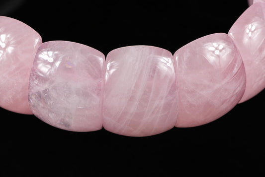 A close-up of a pink rose quartz bracelet with smooth, rounded beads on a dark surface.