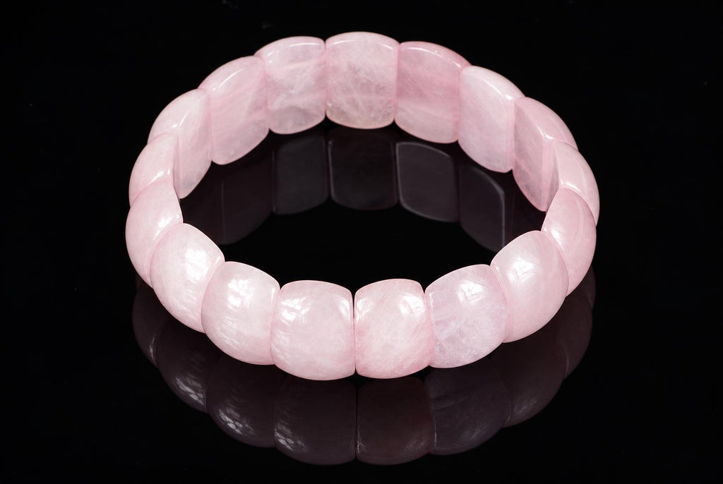 A pink rose quartz bracelet with smooth, rounded beads arranged in a circle on a dark reflective surface.