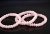 Three pink roundelle bead bracelets lie on a dark reflective surface.
