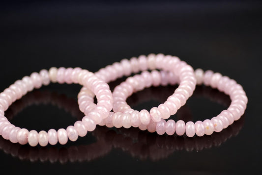 Three pink roundelle bead bracelets lie on a dark reflective surface.