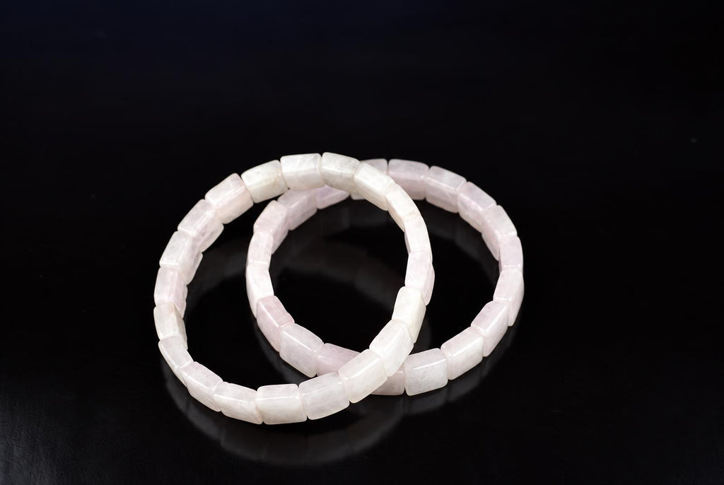 Two square rose quartz bracelets on a dark surface.