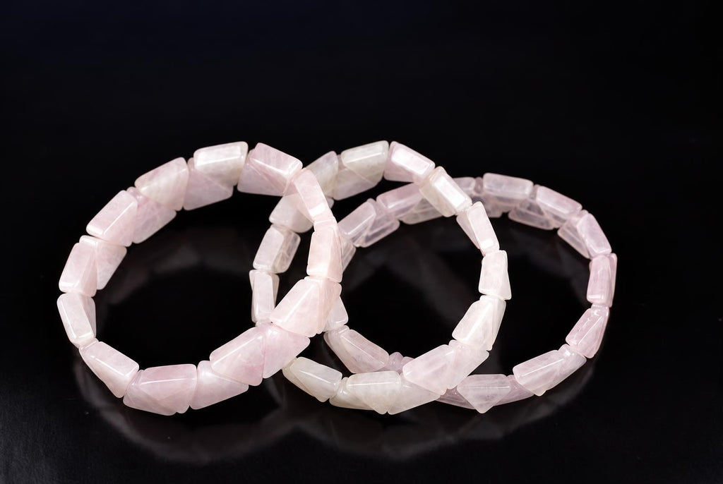 Three rose quartz bracelets with triangular beads lie on a dark surface.