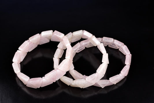 Three rose quartz bracelets with triangular beads lie on a dark surface.