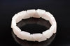 A bracelet made of pale pink, triangular rose quartz stones arranged in a circle on a dark surface.