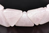 A close-up of a rose quartz bracelet with triangular beads on a dark surface.