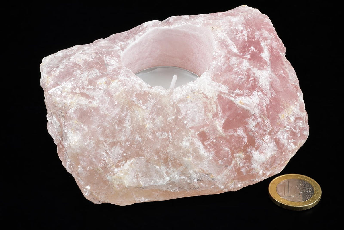 A pink, rough-textured stone candle holder with a central cavity containing a white tea light candle, set against a dark surface.