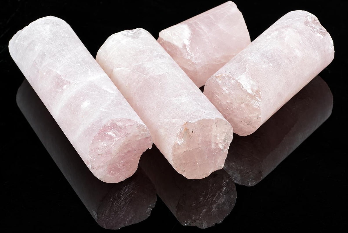 Four pink rose quartz drill cylinders rest on a dark, reflective surface.