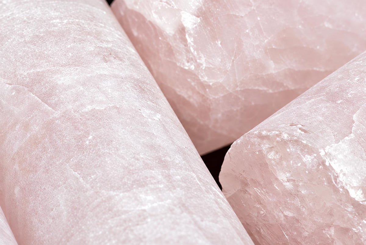 Three pink rose quartz drill cylinders with rough, crystalline surfaces arranged on a dark surface.