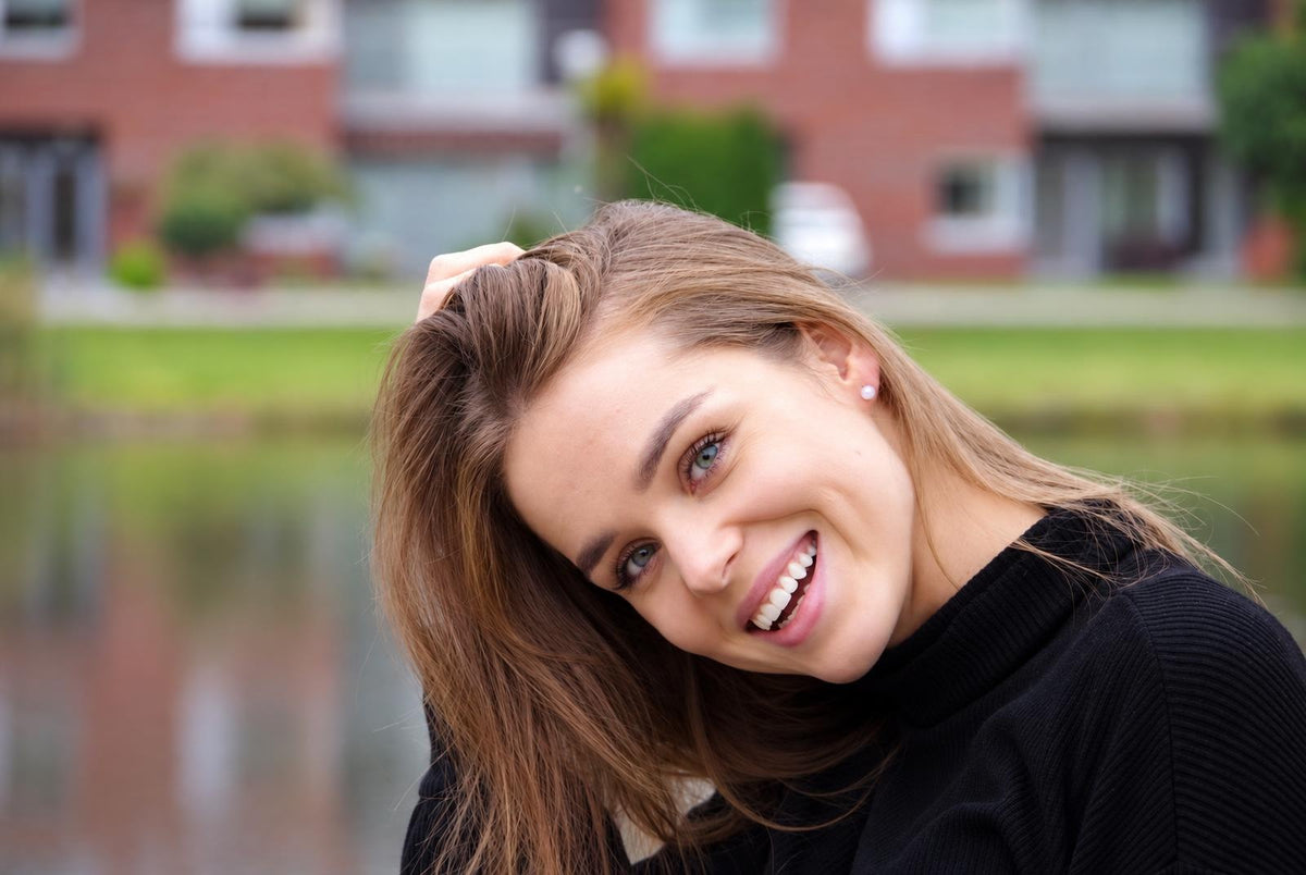 A smiling woman with brown hair and blue eyes, wearing a black top and a small white pearl earring.