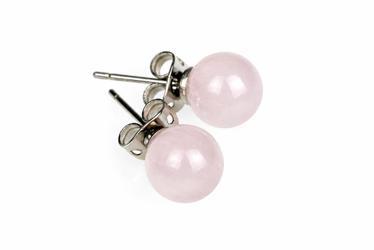 A pair of round, pale pink stud earrings with silver-toned posts and butterfly backs on a white surface.