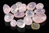 A collection of polished rose quartz stones in pink and clear shades, arranged on a dark reflective surface with a one euro coin for scale.