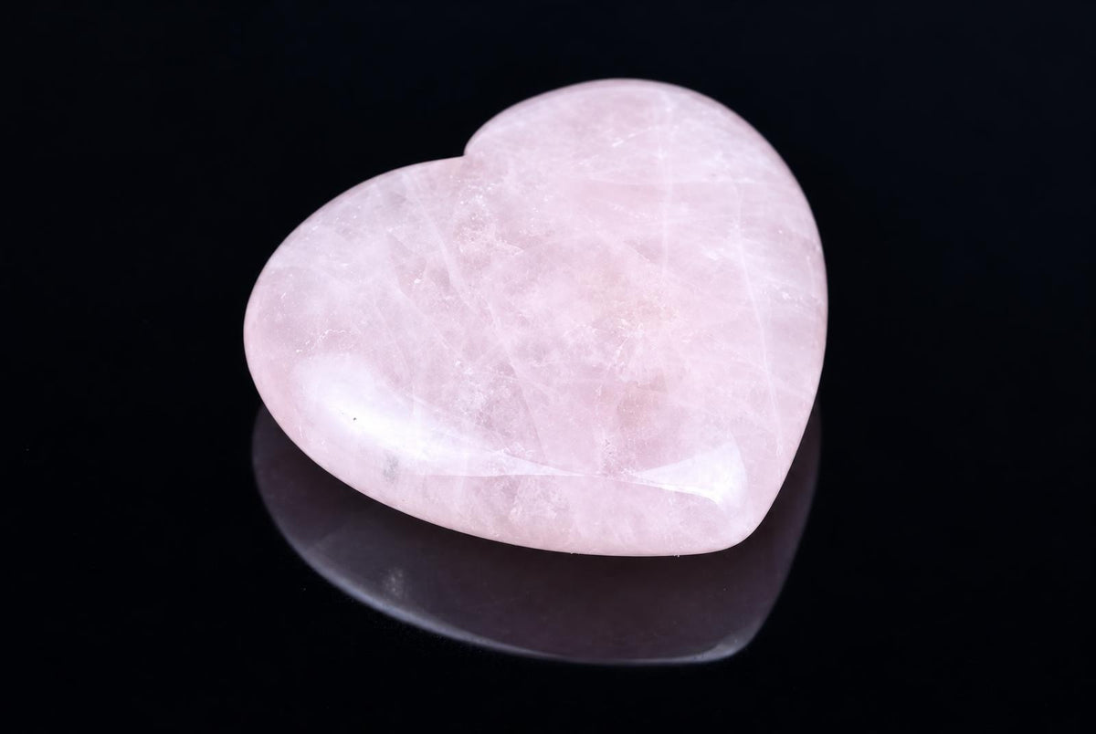 A polished, heart-shaped pink stone rests on a dark, reflective surface.