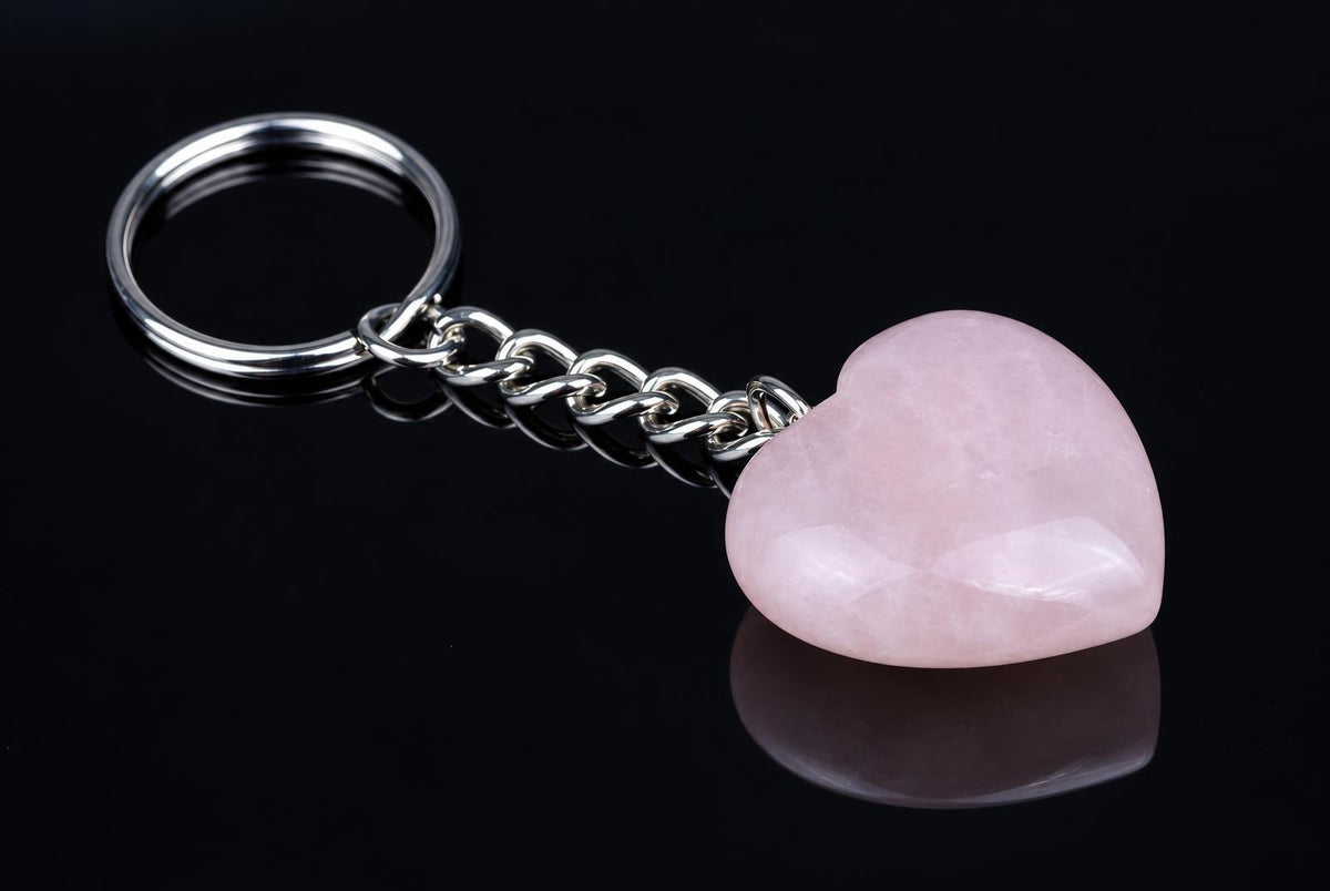 A silver-toned keychain with a polished pink heart-shaped stone on a dark reflective surface.