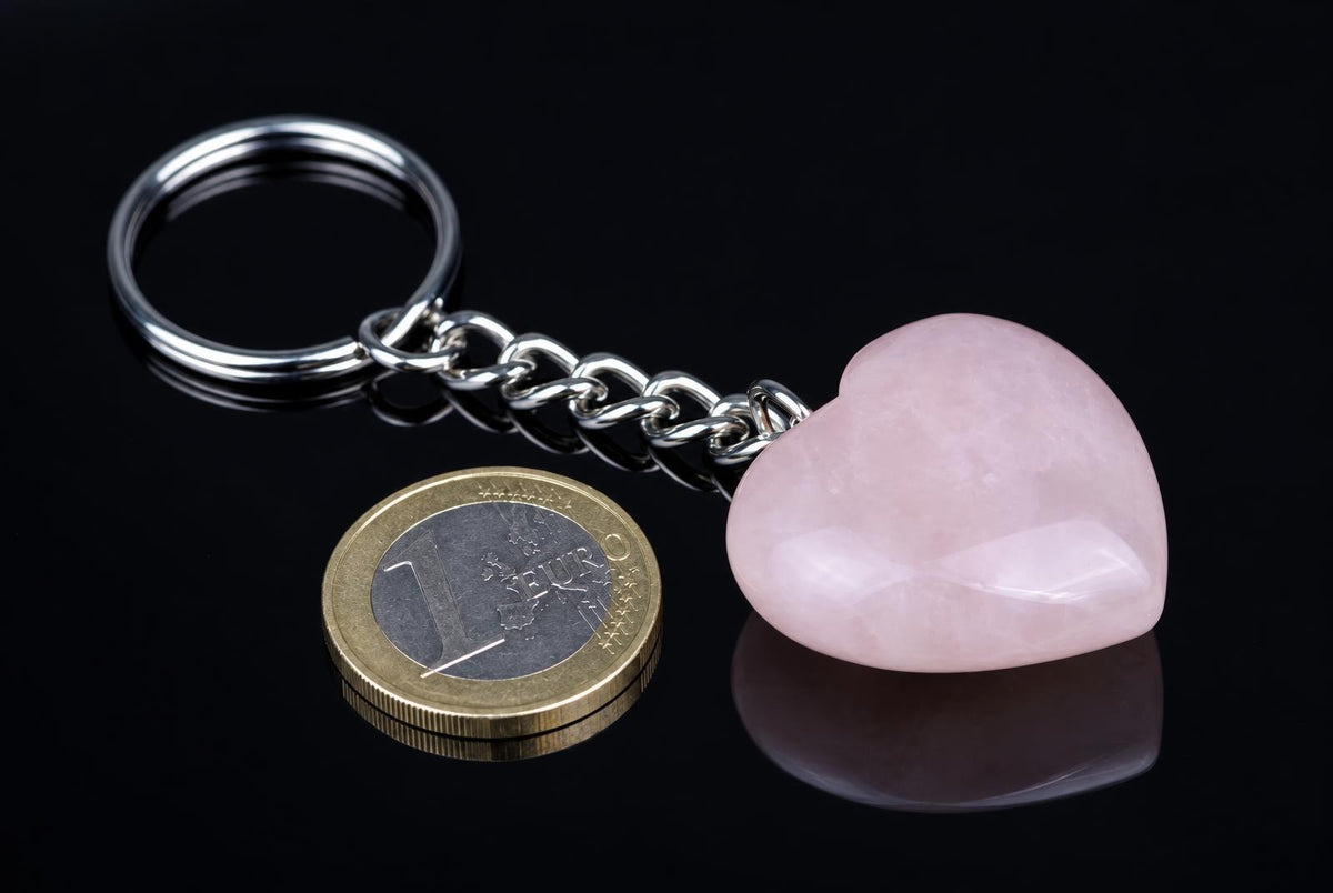 A silver-toned keychain with a pink heart-shaped stone pendant and a metal chain, resting on a dark reflective surface.