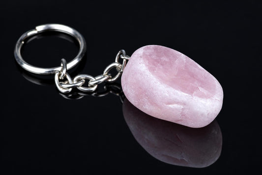 A silver-toned keychain with a smooth, pink stone pendant on a dark reflective surface.
