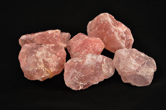 Six raw rose quartz crystals with pink and white surfaces on a dark surface.