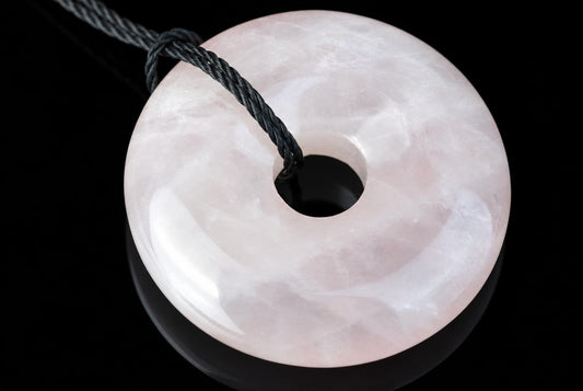 A polished, pale pink donut-shaped pendant with a central hole, threaded on a dark cord against a black background.
