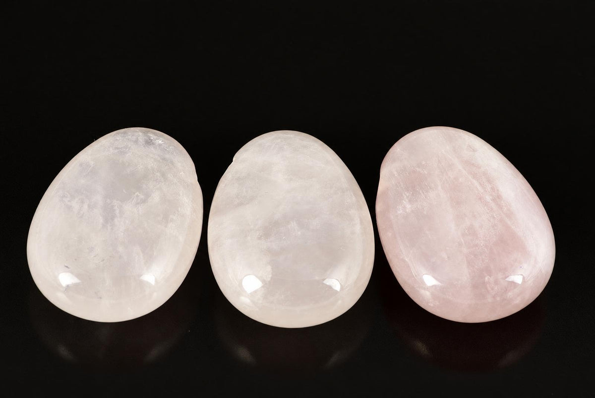 Three polished, smooth stones in white and pink hues arranged on a dark surface.