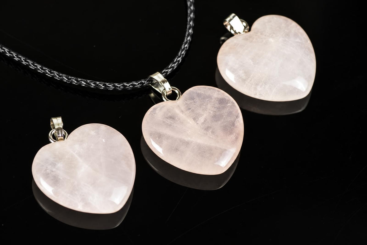 Three heart-shaped rose quartz pendants with silver-toned bail on a dark surface, one attached to a black braided cord.