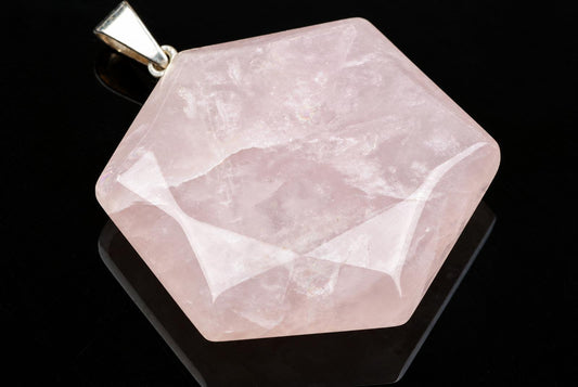 A hexagonal rose quartz pendant with a silver-toned bail rests on a dark surface.