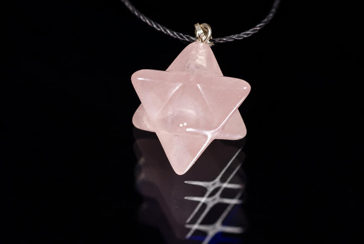 A pink, translucent star-shaped pendant hangs from a dark cord against a black reflective surface.