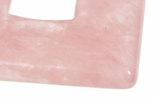 A close-up of a smooth, pink rose quartz pendant with a square cutout and rounded edges on a white surface.