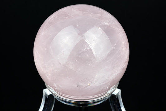 A polished pink rose quartz sphere rests on a clear stand against a dark background.