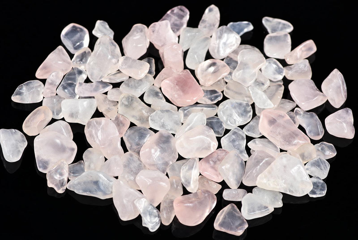 A pile of small, tumbled rose quartz stones in pale pink and clear tones on a dark surface.