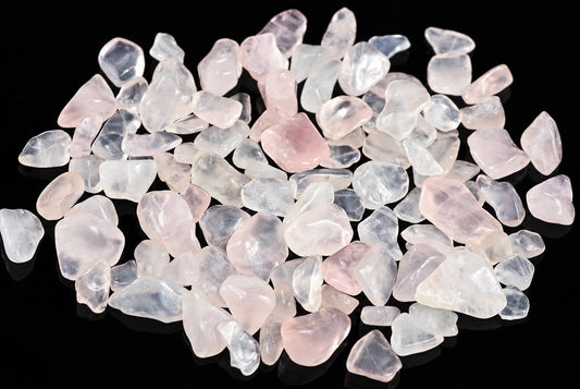 A pile of small, tumbled rose quartz stones in pale pink and clear tones on a dark surface.