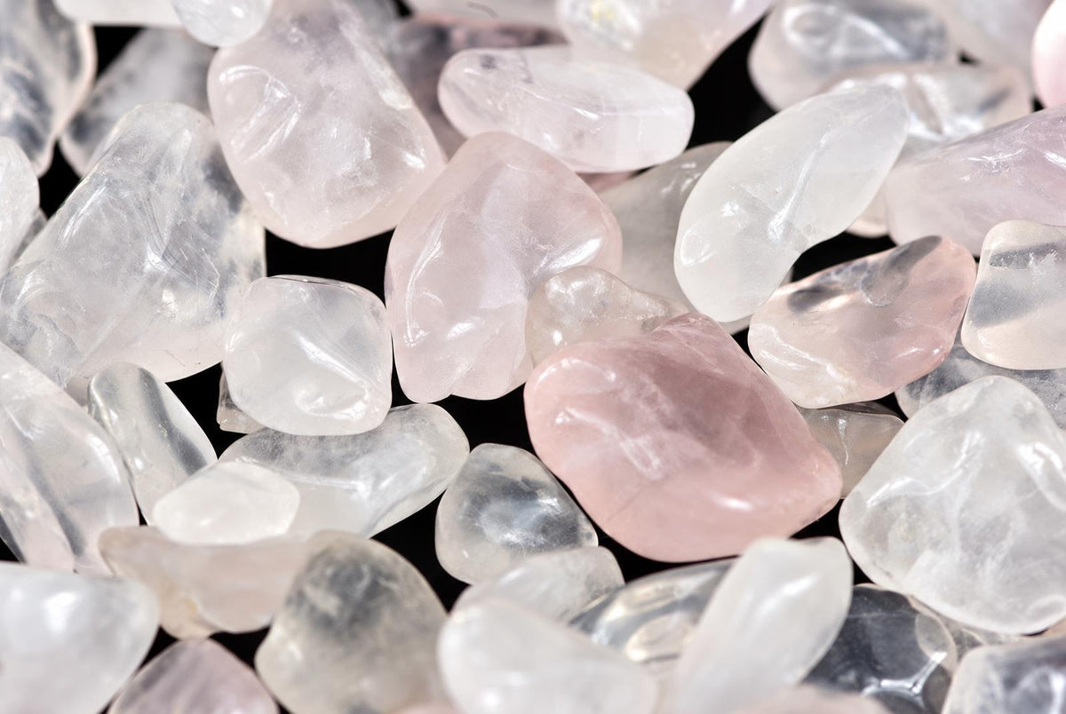 A pile of smooth, polished rose quartz stones in pale pink and white on a dark surface.