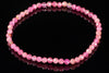 A bracelet of faceted pink beads in varying shades, arranged in a circle on a dark reflective surface.