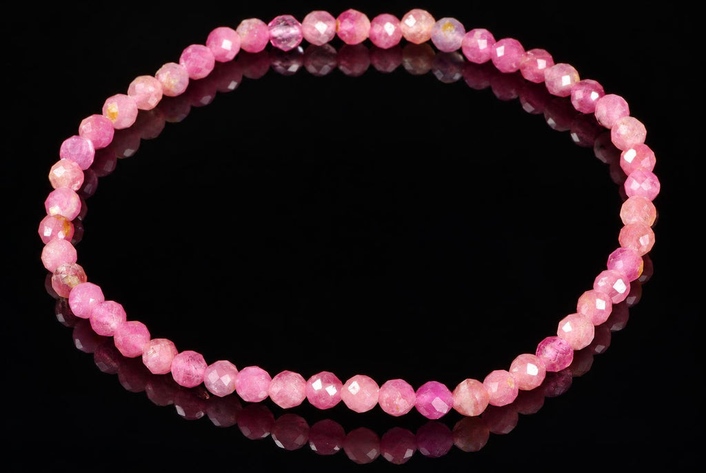 A bracelet of faceted pink beads in varying shades, arranged in a circle on a dark reflective surface.
